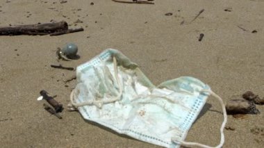 Keşiş yengecinin yavaş ilerleyişi tıbbi atıkların yanında plastik bir tüp taşır, çöpleri maskeler. Coronavirus covid-19 kirlilik ortamı. Plaj Dan sahiline atılmış ameliyat maskesi.