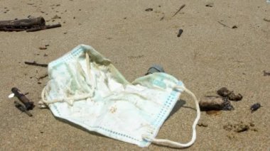 Kullanılmış tıbbi maske çöpünün yanında elinde tüp plastikle inzivaya çekilmiş bir yengeç yürüyor. Kötü sonuçlar doğanın kirlenmesi ya da kirlenmesi. Çevre ve sahil kirliliği Covid19-Dan