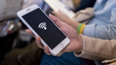 Akıllı telefonu tutan Asyalı kadın ve bedava kablosuz interneti bir uçağın içinde alıyor. Gezgin, uçuş sırasında telefon cihazıyla uçağın içine otur..