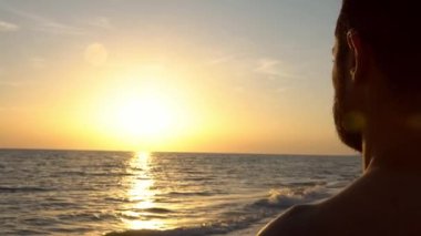 4K, Coronavirus tecridi sırasında güneş batarken güzel plajda tıbbi maskeli beyaz adam. Covid portresi gönder. Salgın için güvenlik maskesi takanlar.