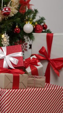 Modern bir Noel ağacının altında, Noel süsleriyle süslenmiş, beyaz bir arka planı olan bir evde, dikey, güzel hediye kutuları yeni yıl için dekor görevi görüyor..