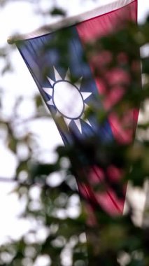 Tayvan bayrağının dikey yavaş hareketi modern bir binanın arka planına ve yemyeşil yapraklara karşı sallanarak kentsel gurur ve mirası temsil ediyor..