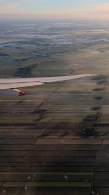 4K, Beautiful aerial of European green land as seen through airplane window in sunset. Airplane over Amsterdam city from above. Flight Netherlands in Europe