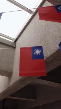 Vertical Taiwan flag flying proudly atop a modern building, set against a clear blue sky, symbolizing national pride and independence.