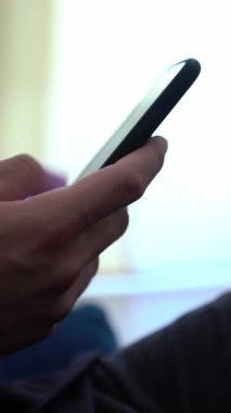 Caucasian man using smartphone, sitting on sofa at home. Male hand touching screen cell phone in the interior house. Surfing internet, checks social network and write text on device mobile