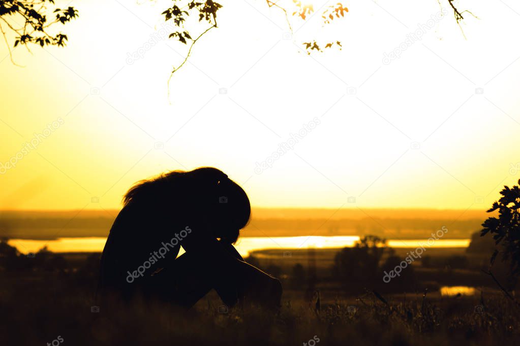 silhouette of a young girl exhausted after physical training, a woman tilted her head to her knees at sunset in the field