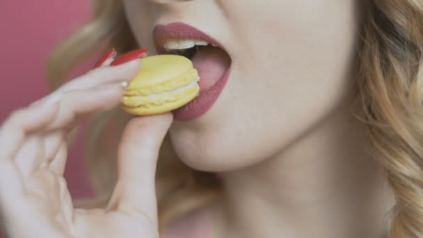 女孩吃一个在彩色背景的开胃马卡龙 一个年轻女子咬饼干 它崩溃 饮食概念 食品工业 — 图库视频影像