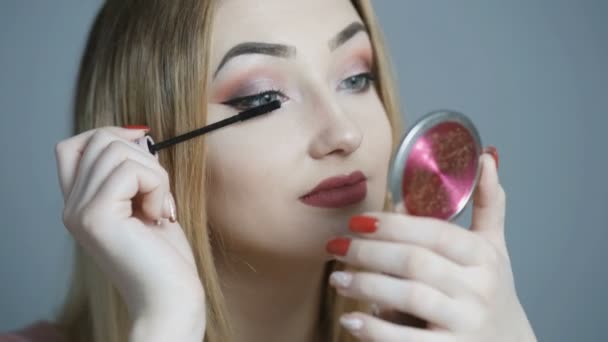美丽的女孩在镜子前化妆 年轻女子用睫毛膏画睫毛 看着镜子上的工作室背景 化妆品和美容的概念 — 图库视频影像