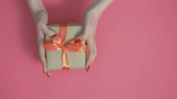 年轻姑娘送给她一份礼物 用欢快的动作把它向前伸展 一个女人高兴地摇着盒子 带着彩色粉红背景的弓 带着节日和感情的概念 — 图库视频影像
