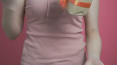 Genç kız, elinde hediye paketi ve hareketlerle elini kaldırdı. Renkli pembe arka planda bir kutuyla mutlu bir şekilde kutuyu sallayan bir kadın. Bayram ve duygu kavramı.