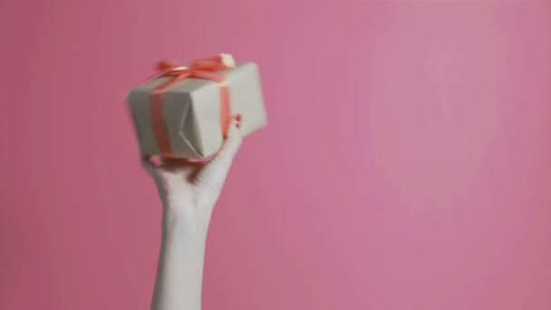 若い女の子は手を挙げて包み紙を持って動きました女性は喜んでピンクの背景に弓で箱を振る休日や感情の概念 — ストック動画
