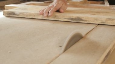 Genç adam ahşap bir tahtayı dairesel testere bıçağıyla kesiyor, ahşap işçiliği için profesyonel bir aletle bir atölye kuruyor, inşaat parçaları üretiminde kullanılan bir inşaat süreci kavramı.