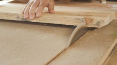 Genç adam ahşap bir tahtayı dairesel testere bıçağıyla kesiyor, ahşap işçiliği için profesyonel bir aletle bir atölye kuruyor, inşaat parçaları üretiminde kullanılan bir inşaat süreci kavramı.