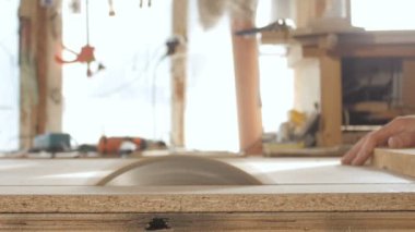 Genç adam ahşap bir tahtayı dairesel testere bıçağıyla kesiyor, ahşap işçiliği için profesyonel bir aletle bir atölye kuruyor, inşaat parçaları üretiminde kullanılan bir inşaat süreci kavramı.