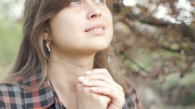 young woman moves lips saying the words of the prayer to God , girl sincere folded her arms on chest garden in spring, the concept of religion and spirituality