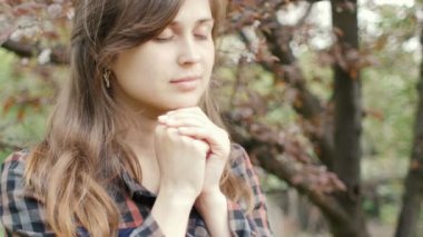 young woman moves lips saying the words of the prayer to God , girl sincere folded her arms on chest garden in spring, the concept of religion and spirituality