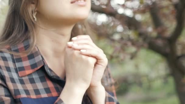 年轻女子摇动着嘴唇 说着向上帝祈祷的话 在春天 女孩真诚地抱着胳膊躺在胸前的花园里 这是宗教和灵性的概念 — 图库视频影像