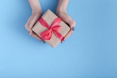 elinde bir hediye tutan kız, bir pastel renkli mavi arka plan, üst görünümü, konsept tatil, sevgi ve bakım elinde bağlı kırmızı kurdele yay ile hediye kutusu ile kadınlar