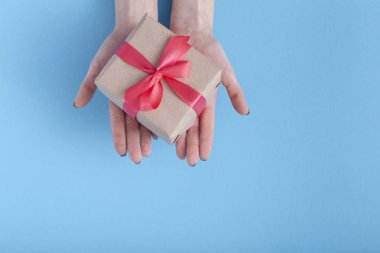 kız avuç içi mevcut ileri ye doğru germek, bir pastel renkli mavi arka plan, üst görünümü, konsept tatil, sevgi ve bakım elinde bağlı bir kırmızı kurdele yay ile hediye kutusu ile kadın