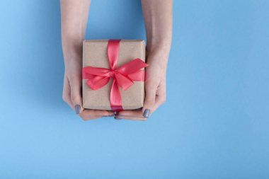 elinde bir hediye tutan kız, bir pastel renkli mavi arka plan, üst görünümü, konsept tatil, sevgi ve bakım elinde bağlı kırmızı kurdele yay ile hediye kutusu ile kadınlar