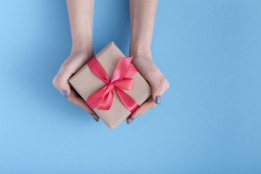 elinde bir hediye tutan kız, bir pastel renkli mavi arka plan, üst görünümü, konsept tatil, sevgi ve bakım elinde bağlı kırmızı kurdele yay ile hediye kutusu ile kadınlar