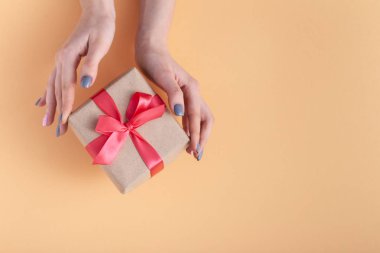 elinde bir hediye tutan kız, elinde hediye kutusu ile kadınlar bir pastel renkli arka plan üzerinde bağlı kırmızı kurdele yay ile dekoratif zanaat kağıt sarılmış, üst görünüm, konsept tatil, sevgi ve bakım