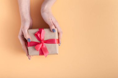 elinde bir hediye tutan kız, elinde hediye kutusu ile kadınlar bir pastel renkli arka plan üzerinde bağlı kırmızı kurdele yay ile dekoratif zanaat kağıt sarılmış, üst görünüm, konsept tatil, sevgi ve bakım