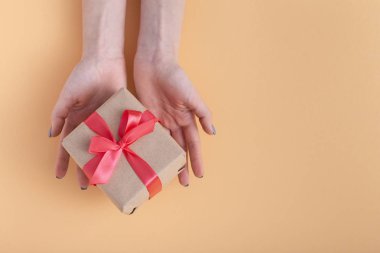 elinde bir hediye tutan kız, elinde hediye kutusu ile kadın bir pastel renkli arka plan üzerinde bağlı kırmızı kurdele yay ile dekoratif zanaat kağıt sarılmış, üst görünüm, konsept tatil, sevgi ve bakım