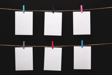 siyah bir arka plan üzerinde keten halat üzerinde renkli clothespins ile bağlı boş kağıt kartları, boş şablonlar konsept ofis ve fotoğraf endüstrisi, dekor