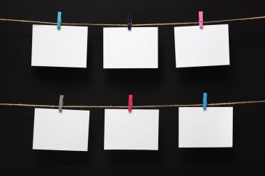 siyah bir arka plan üzerinde keten halat üzerinde renkli clothespins ile bağlı boş kağıt kartları, boş şablonlar konsept ofis ve fotoğraf endüstrisi, dekor