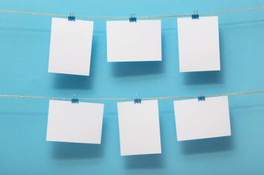 yaşam anlarının fotoğraf kartları için yer, mavi arka plan üzerinde kırtasiye klipleri ile keten bir ipe bağlı boş boşluklar, metin için bir kavram şablonu, görüntüler, ev dekorasyonu için fikir