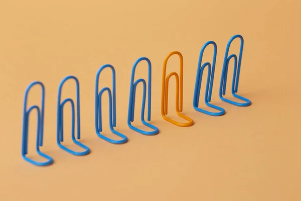 Orange clip among the blues, unlikeness to others, the concept of individuality, optimism, creative idea with office paper clips, concept of psychology — Stock Photo, Image