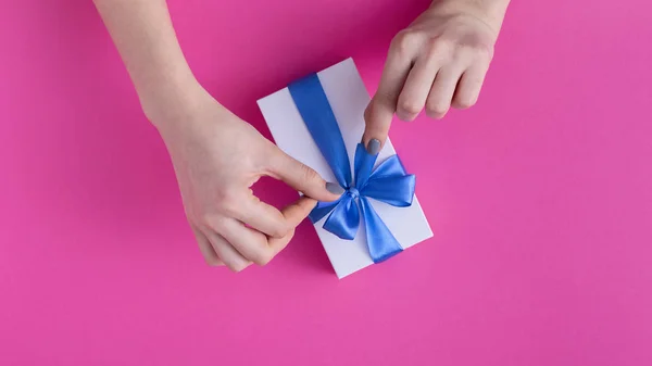 Menina segurando um belo presente nas mãos, mulheres com caixa de presente com um laço de fita azul amarrado nas mãos em um fundo de papelão rosa colorido, vista superior, férias conceito, amor e cuidado — Fotografia de Stock