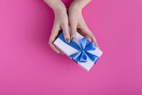 Menina segurando um belo presente nas mãos, mulheres com caixa de presente com um laço de fita azul amarrado nas mãos em um fundo de papelão rosa colorido, vista superior, férias conceito, amor e cuidado — Fotografia de Stock