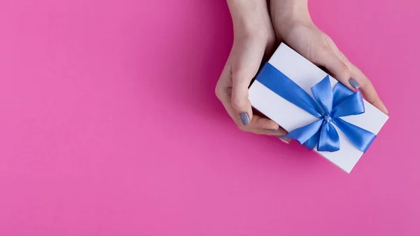 Κορίτσι κρατώντας ένα όμορφο δώρο στα χέρια, γυναίκες με κουτί δώρου με ένα δεμένο μπλε κορδέλα τόξο στα χέρια σε ένα χρωματιστό ροζ φόντο από χαρτόνι, κορυφή θέα, concept διακοπές, αγάπη και φροντίδα — Φωτογραφία Αρχείου