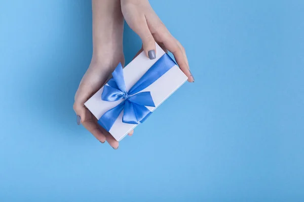 Menina segurando um belo presente nas mãos, mulheres com caixa de presente branco com um laço de fita azul amarrado nas mãos em um fundo de cor pastel, vista superior, férias conceito, amor e cuidado — Fotografia de Stock