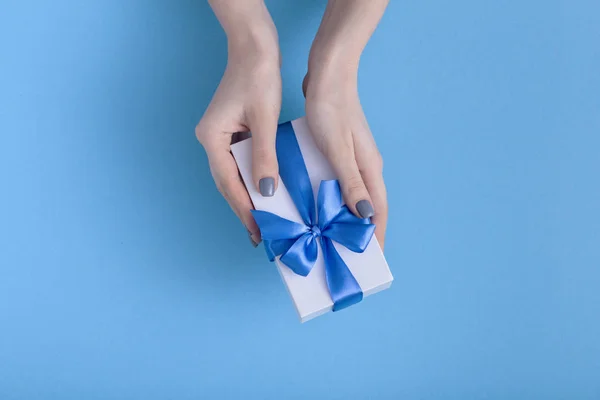 Menina segurando um belo presente nas mãos, mulheres com caixa de presente com um laço de fita azul amarrado nas mãos em um fundo de cor pastel, vista superior, férias conceito, amor e cuidado — Fotografia de Stock