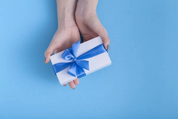 Meisje stretch vooruit op de palmen aanwezig, vrouwen met gift box met een gebonden blauw lint Bow in handen op een Pastel gekleurde achtergrond, Top uitzicht, concept vakantie, liefde en zorg — Stockfoto