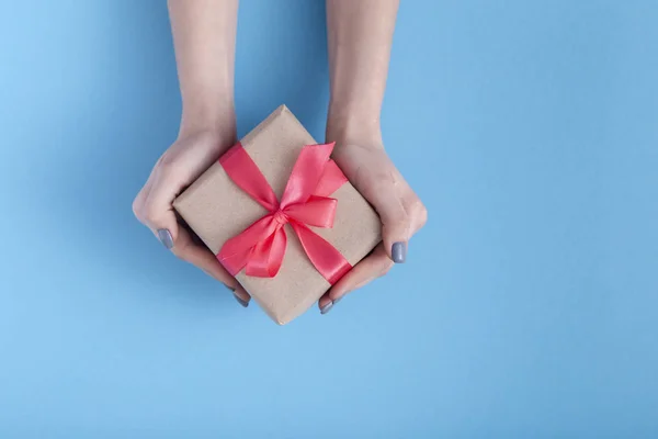 Menina segurando um presente em mãos, mulheres com caixa de presente com um laço de fita vermelha amarrada em mãos em um fundo azul de cor pastel, vista superior, férias conceito, amor e cuidado — Fotografia de Stock