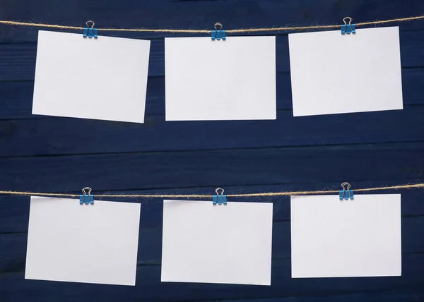 empty paper cards attached with colorful clips on linen rope on the background of in blur wooden blue board, blank templates for images or text, concept photo wall