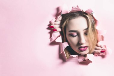 pembe karton kağıt bir delik yırtılma genç bir kadının moda portresi, makyaj ile bir kızın yüzü, moda yaratıcı konsept özgürlük, gençlik yaşam tarzı