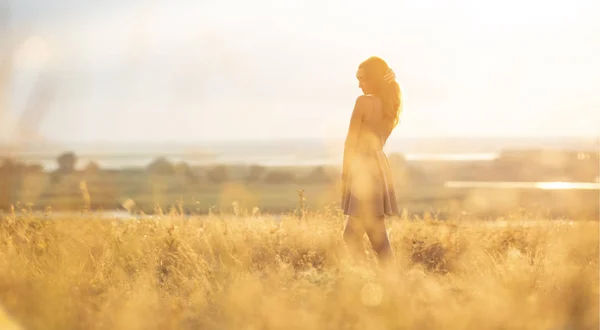 Chica de ensueño en un campo al atardecer, una mujer joven en una neblina del sol disfrutando de la naturaleza, estilo romántico — Foto de Stock