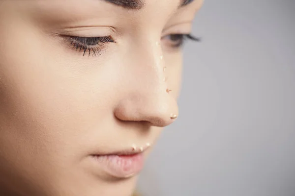 Parte da cara de mulher jovem com gotas de cosmético no nariz, menina bonita fazendo uma maquilagem no fundo do estúdio, conceito de cosméticos e beleza natural — Fotografia de Stock