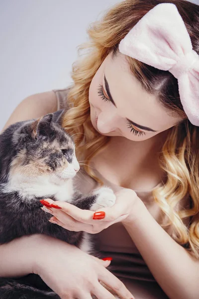 Retrato de una hermosa chica linda con un gato en las manos, mujer joven en una diadema para maquillaje en un fondo de estudio gris con un gatito, concepto de belleza natural, cosméticos, cuidado del cuerpo —  Fotos de Stock