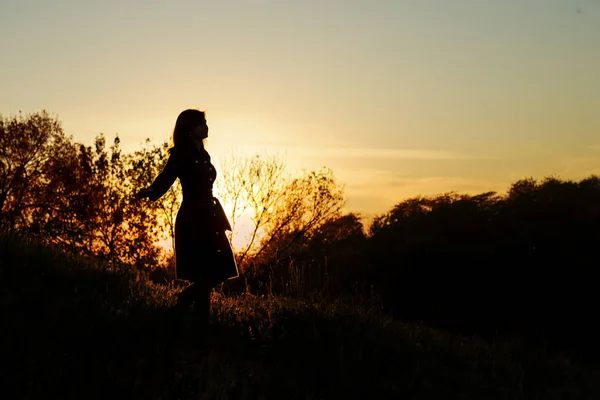 Silueta de una joven descendiente de una colina al atardecer, una niña caminando en el otoño en el campo —  Fotos de Stock