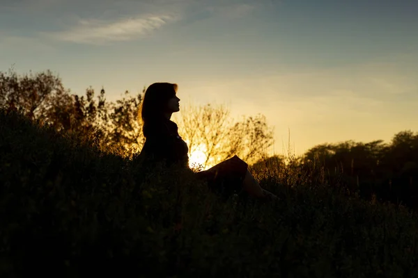 夕暮しの丘の上に座っている若い女性のシルエット、秋の風景の中の女の子の姿 — ストック写真