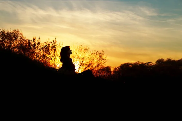 Silhouette di una giovane donna seduta su una collina al tramonto, una ragazza che cammina in autunno nel campo — Foto Stock