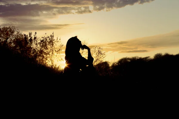 Silhouette di una giovane donna seduta su una collina al tramonto, una ragazza che cammina in autunno nel campo — Foto Stock