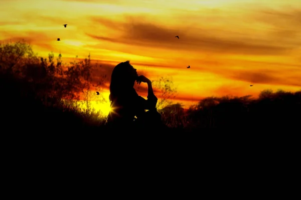 Silhouette of a young woman sitting on a hill at sunset, a girl dreaming, looking at the sky as birds fly and meditates — Stock Photo, Image
