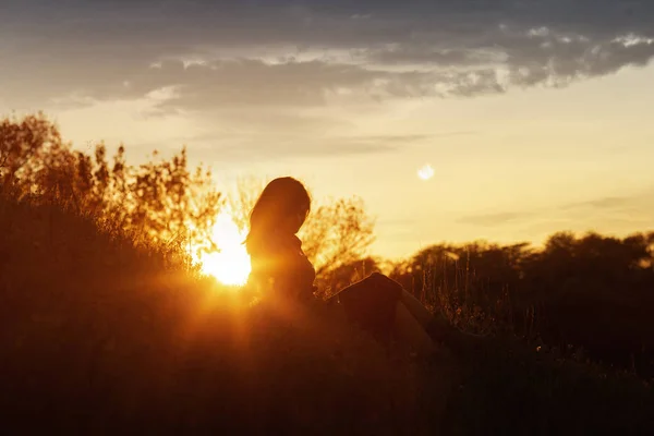 Silhouette di una giovane donna seduta su una collina al tramonto, una ragazza che cammina in autunno nel campo — Foto Stock